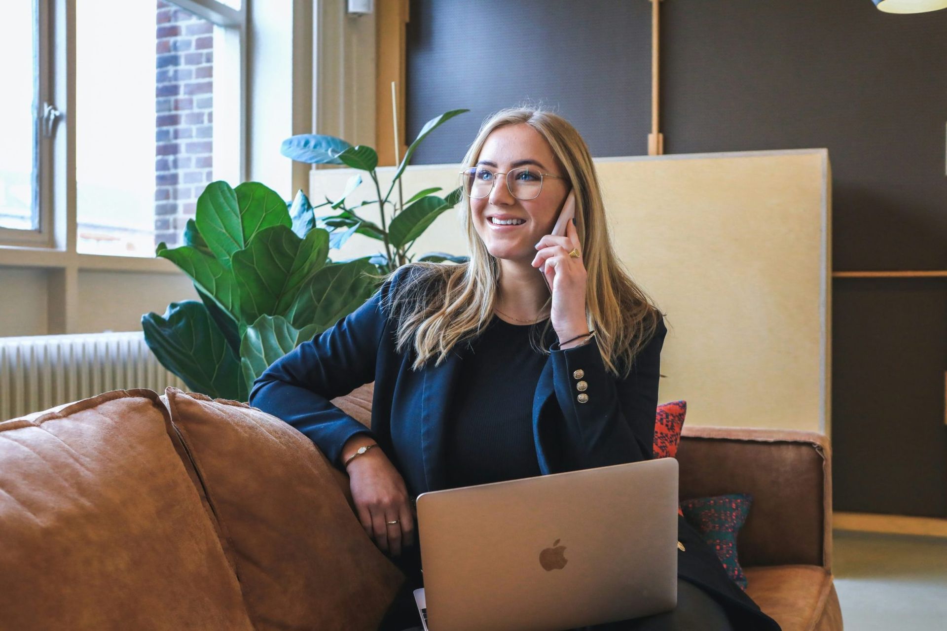 A woman comfortably sitting on a couch, multitasking with a laptop and a phone call.